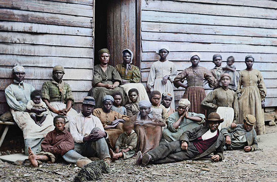 Black people. An archival photo showing more than a dozen Black people of various ages and gender in front of a cabin.