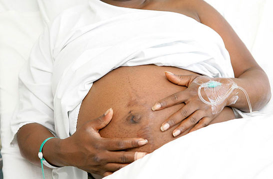 Black pregnancy. Black woman lying in white sheets holding an exposed pregnant belly.