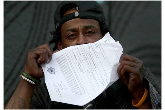 Black man with backwards cap, 30s, holding eviction papers in front of his face. Only his eyes are showing. 