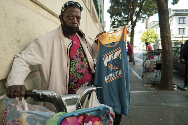 Damon walks his bicycle down a busy sidewalk in the Tenderloin neighborhood in late June, selling Warrior jerseys for $7. He packs his merchandise on his bike, which he used for transportation to avoid public transit and the coronavirus, he said. Yesica Prado/San Francisco Public Press