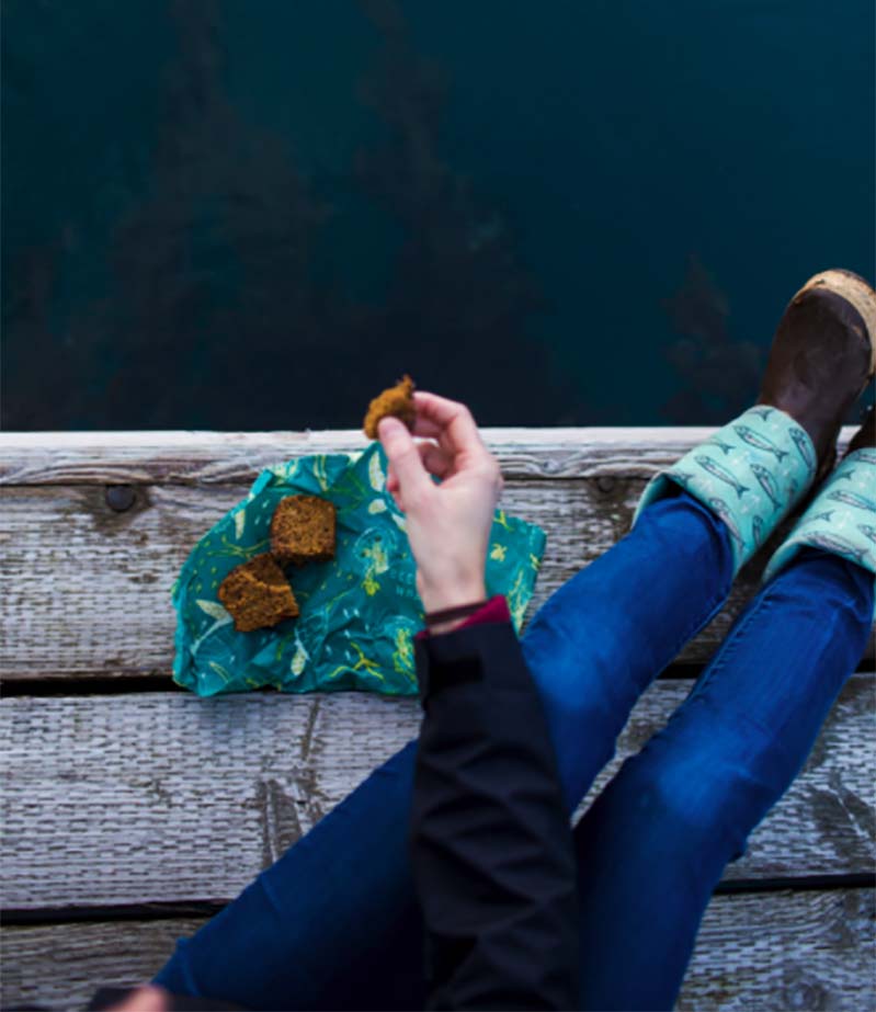 Woman sitting on dock eating a snack from a bee''s wrap reusable food wrap