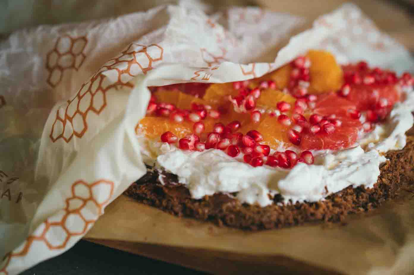 Bread with cream cheese and fruit on table next to orange slice on top of bee''s wrap