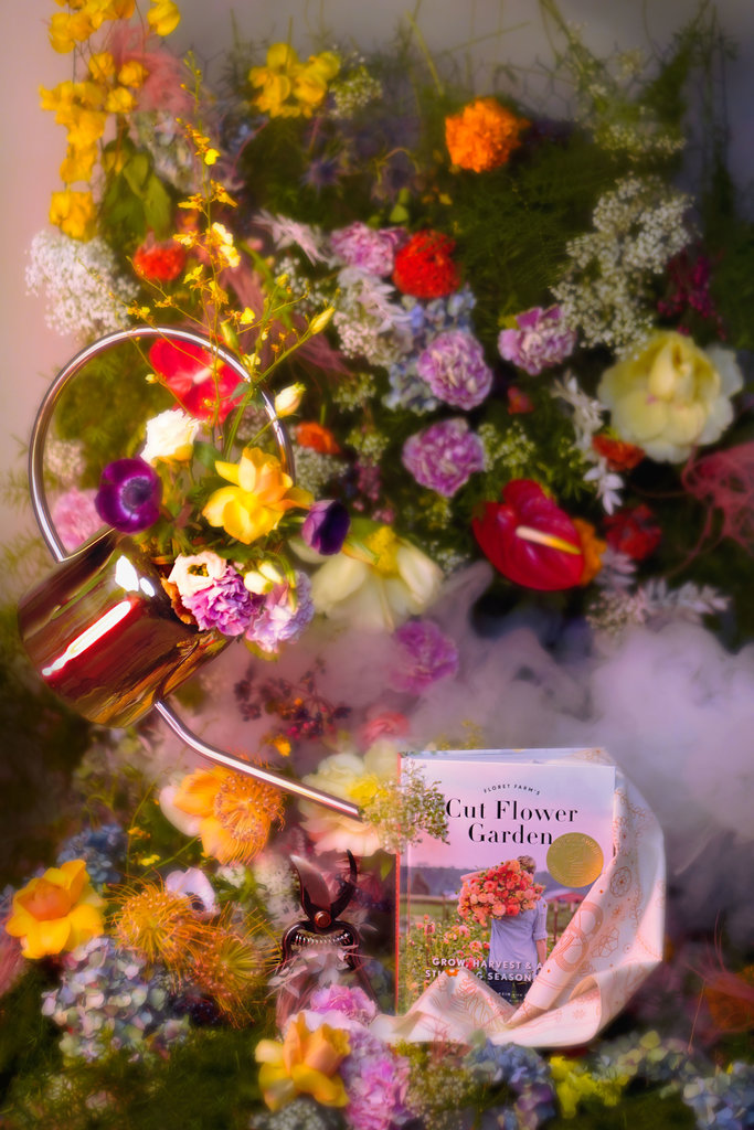 A soft floral forest shows a copper watering can, Floret Farms book, tan Asrai Garden bandana and Barebones pruners surrounded by a cloud of smoke.