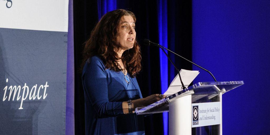Executive Director Meira Neggaz speaking at a podium