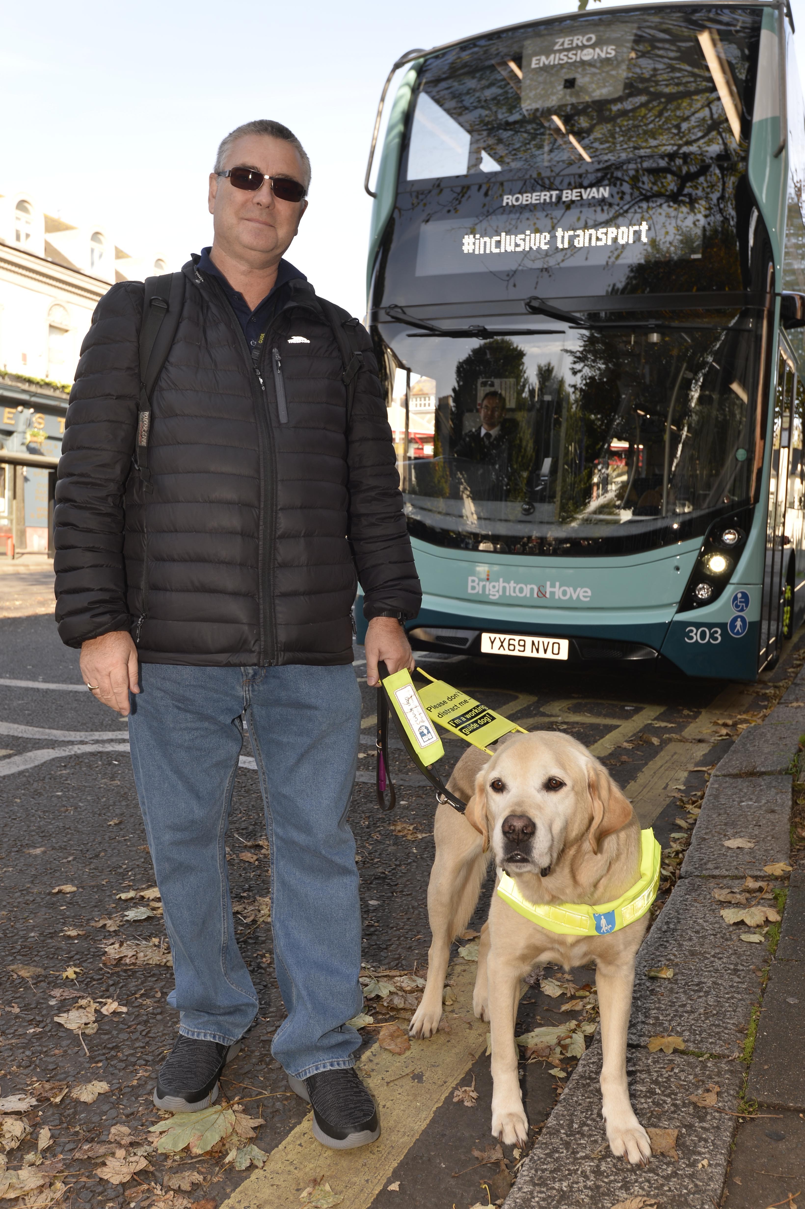 Man with guide dog stood in front of a bus