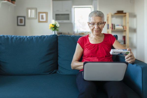 Lady sitting on couch with laptop looking at medication