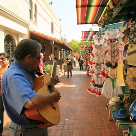 A latinx man plays a guitar in a marketplace setting
