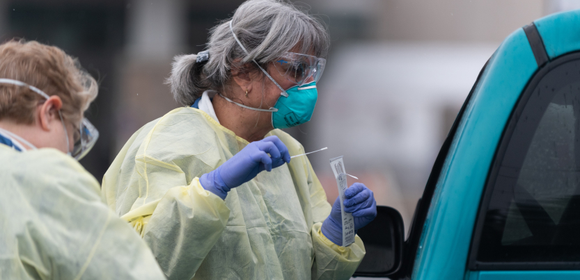 masked gloved gowned worker adminsters virus test at car window