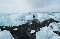 a scientist appears small next to sea ice that has come aground on the shoreline, with the ocean awash in ice beside him