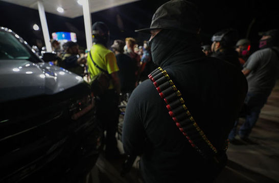 Kenosha Armed White Man. Back of white man standing in gas station wearing a hat, face covering and bullets across shoulder.