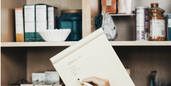 Hands holding notebook and pen in front of pantry - image