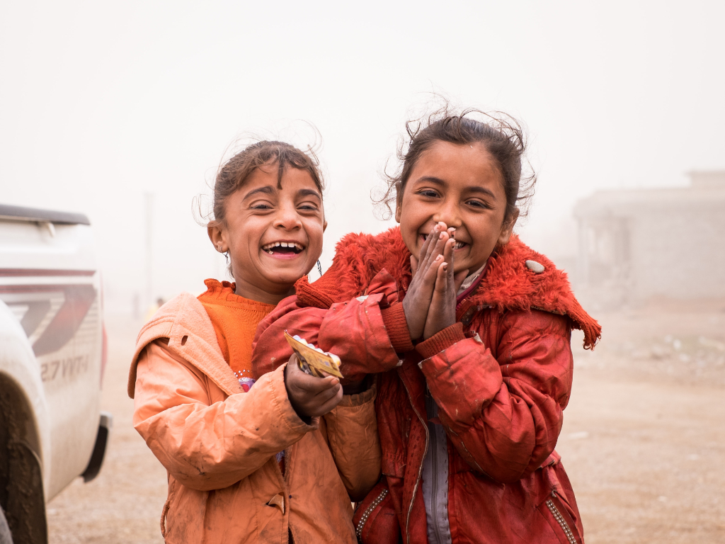 Two children laughing next to car.