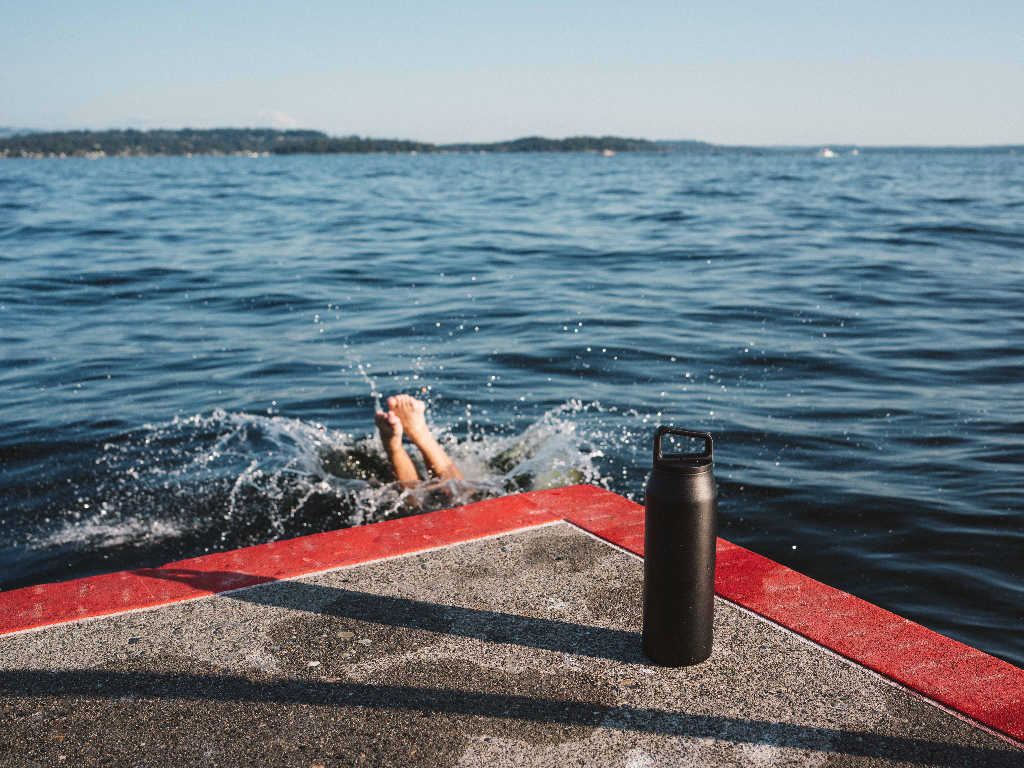 Person jumping into lake next to 32oz Wide Mouth Bottle in Black.