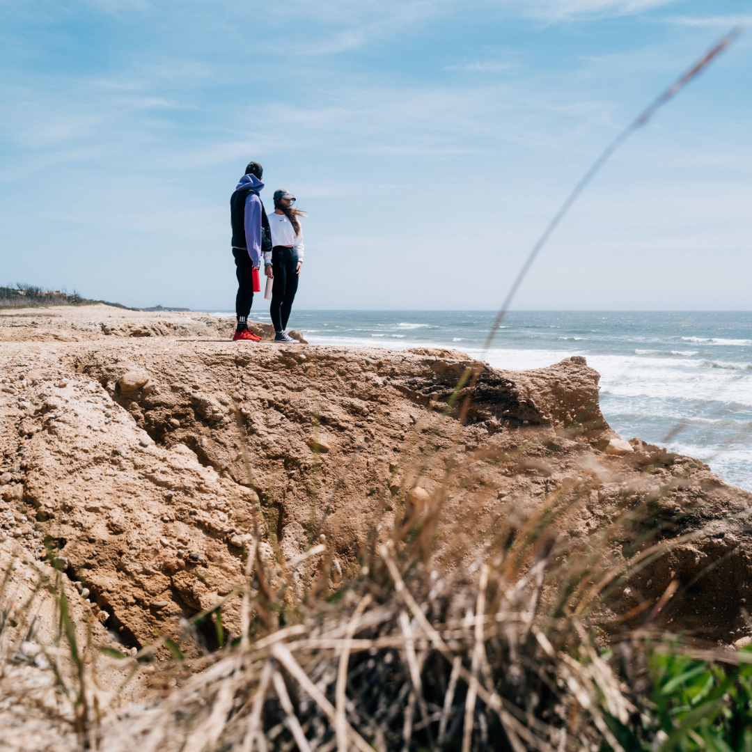 Two people standing on a beach cliff holding MiiR drinkware.