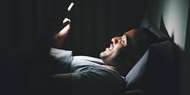 Man smiling while looking at cell phone at night - Image