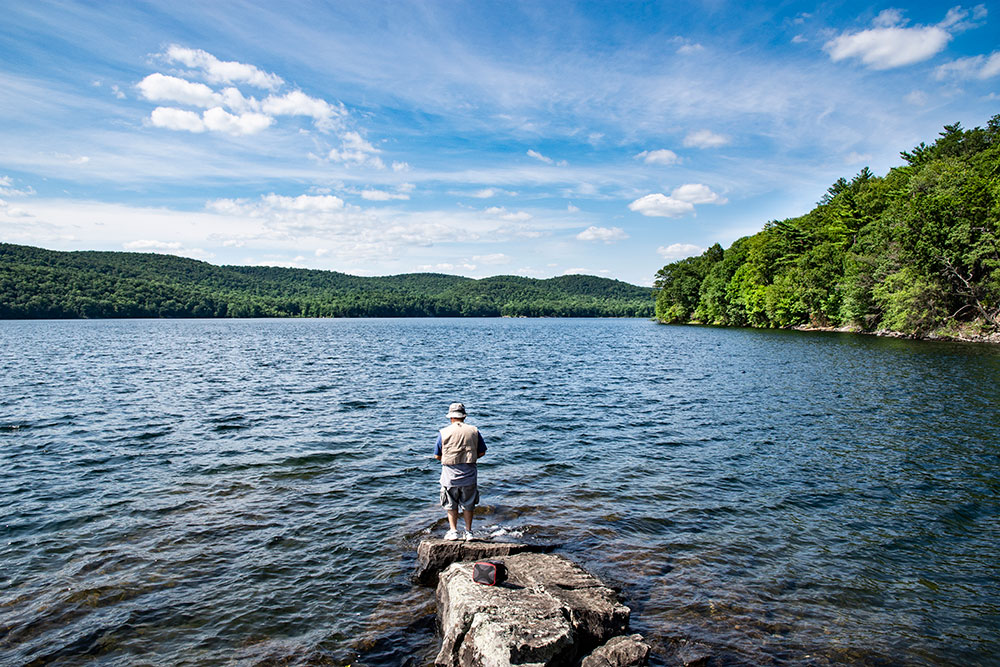 A man in fishing attire on the rocky shore of a lake