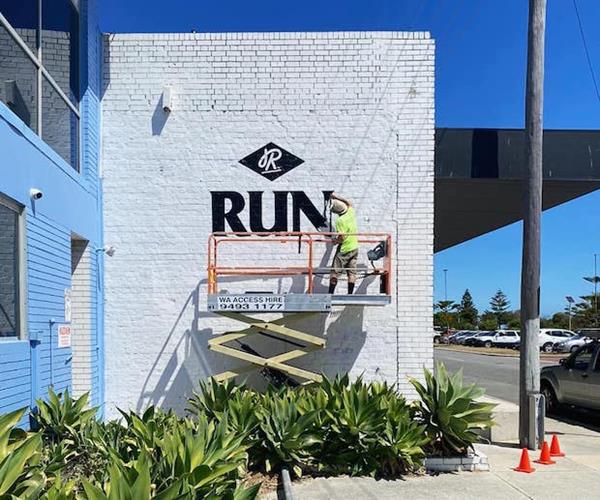 Black 'Run' sign being painted on white brick wall.