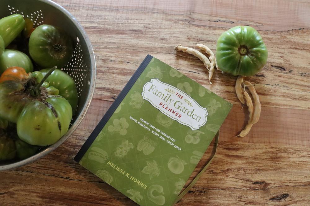 The Family Garden Planner book sitting on a table with a bowl of green tomatoes sitting
next to it.
