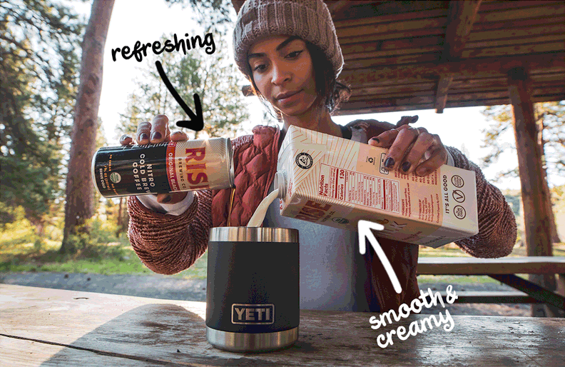 Photo of woman outdoors pouring Rise original black coffee and organic oat milk into a cup.