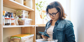 Woman checks list on her phone in front of a pantry - Image