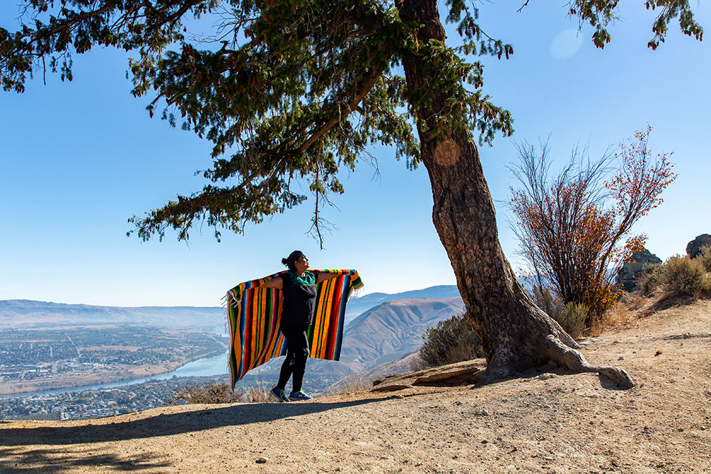 A woman wearing a colorful blanket walks on a ridge under a tree