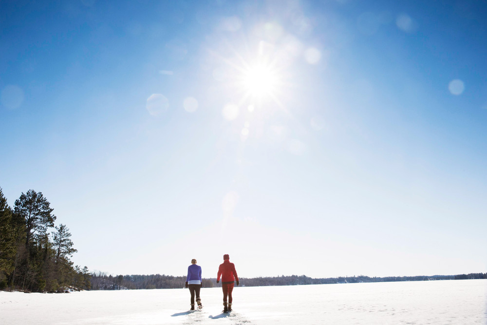 Two women snowshoe across a frozen lake surface