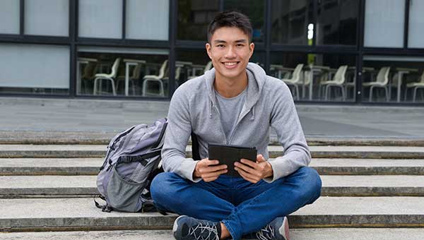 image: student sitting on steps with backpack and ipad