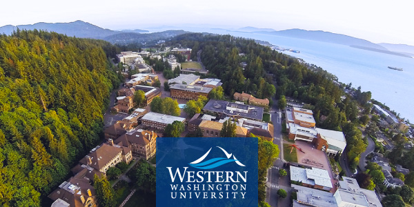 Western Washington University from drone. Brick buildings surrounded by forest on one side and the bay on the other. Islands and mountains in the distance.