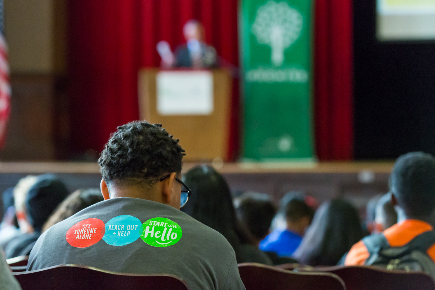 A student with the three steps of Start With Hello on his shirt listens to a presentation.