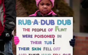 Young Black girl wearing a pink hat and matching pink coat holds a sign protesting the Flint water crisis in Flint, Michigan.