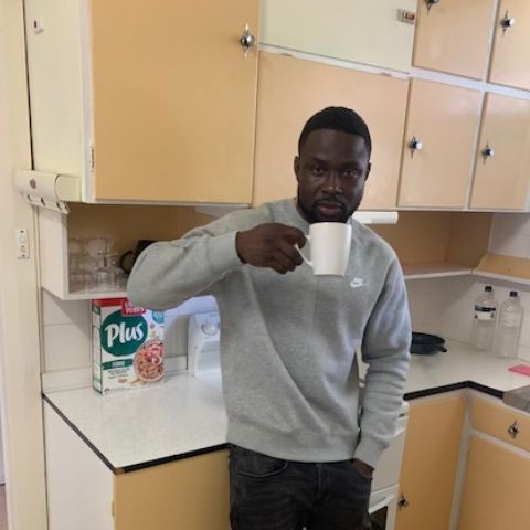 Emmanuel holds cup of tea in his kitchen
