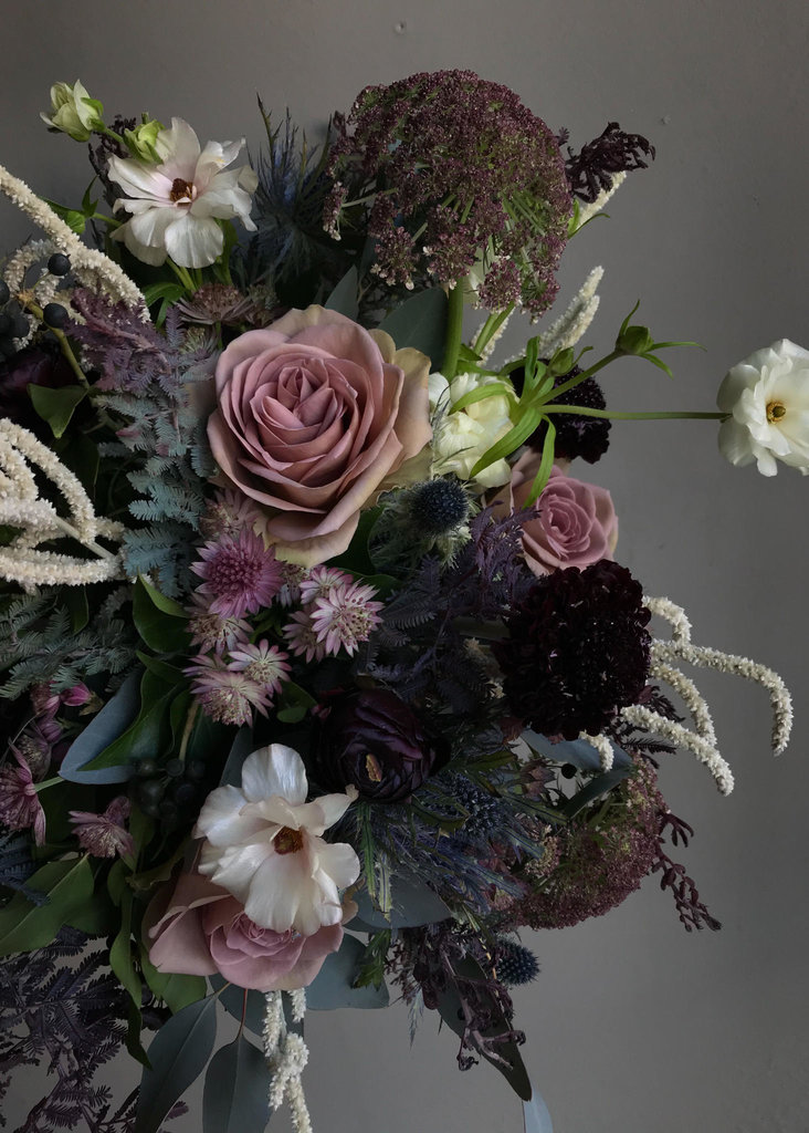 Mauves and berry tones are the theme to this beautiful Asrai arrangement. Dusty purple roses sit amongst chocolate Queen Anne''s lace, silvery Butterfly Ranunculus and dark Scabiosas. 