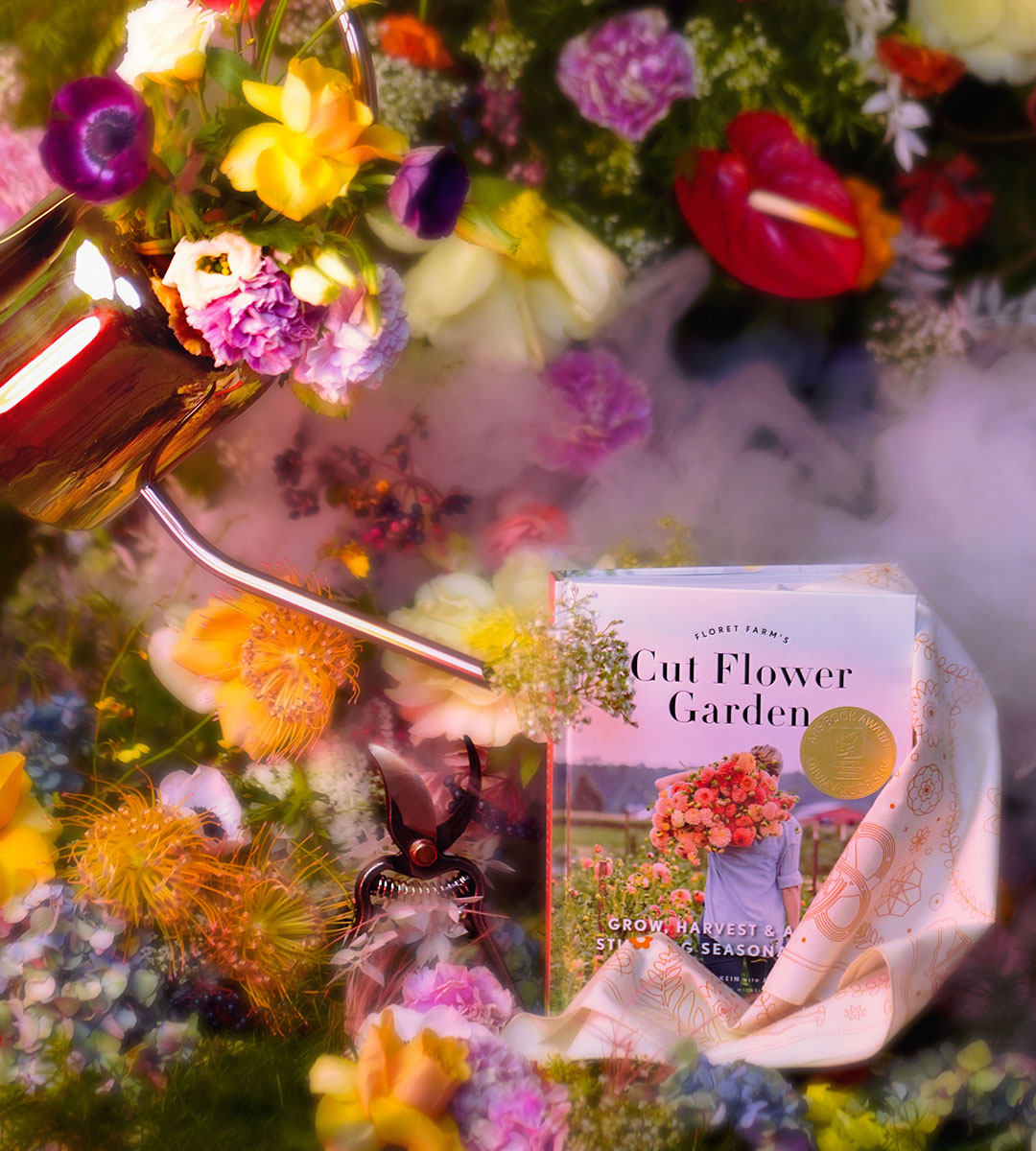 A gorgeous fairy floral backdrop features a copper watering can pantomiming pouring from the corner of the picture. A tan Asrai Garden bandana flows out of the Floret Farms Cut Flower Garden book while the barebones pruners stand center photo.