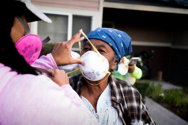 A volunteer places places an N95 mask on a woman. Courtesy Mask Oakland