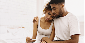 Man and woman sitting on bed looking at early pregnancy test - Image