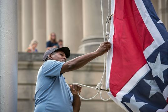 Black Man pulling strings on Mississippi State Flag outside Capitol Building 