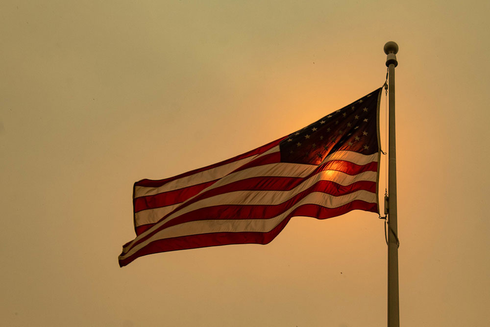 An American flag flies against a smoky sky