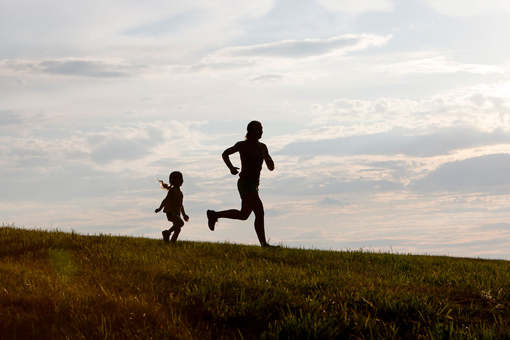 Silhouette of a mom and daughter running on a hillside