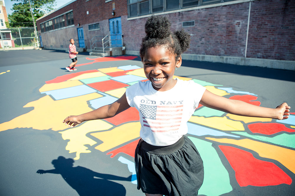 A school-aged girl smiles in front of a ground mural of the United States map