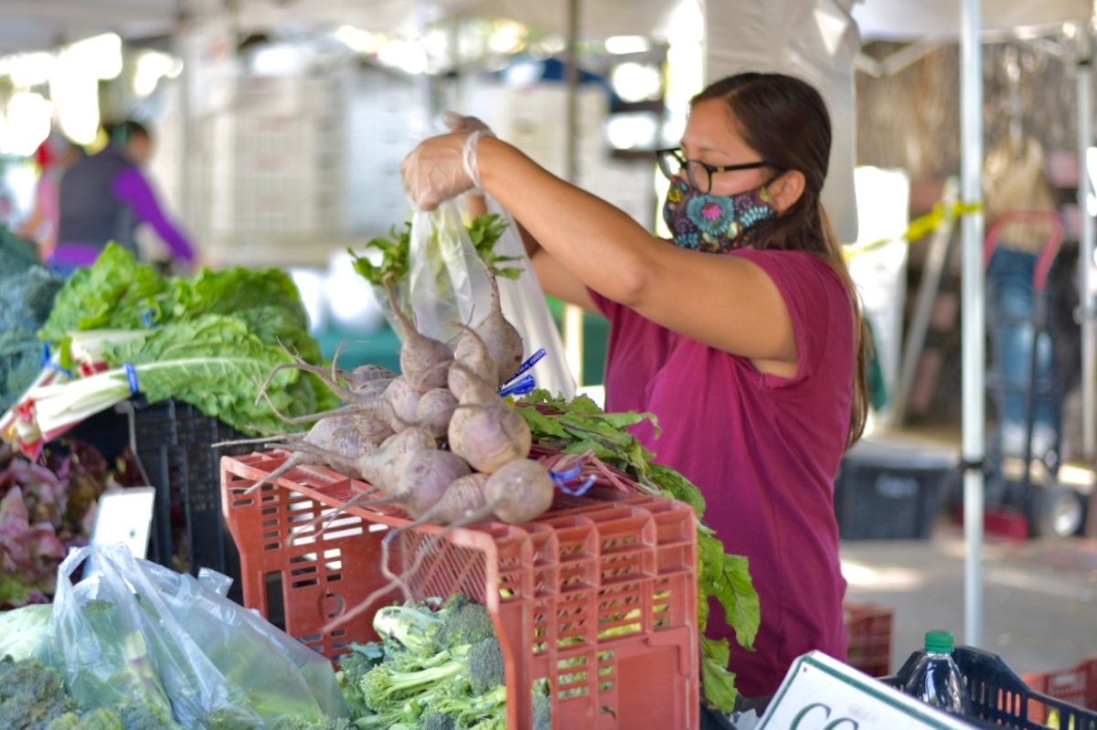 Woman selecting vegetables at farmers'' market with mask
