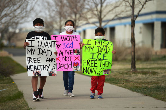 three Latinx children a boy, 10, a girl, 11, a boy six, hold signs in front of them like "I don''t want my dad free and healthy"