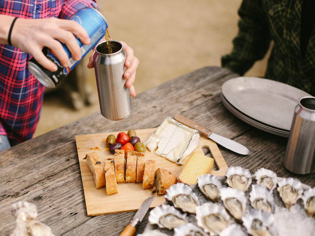 Person pouring drink into Tall Boy at outdoor picnic.