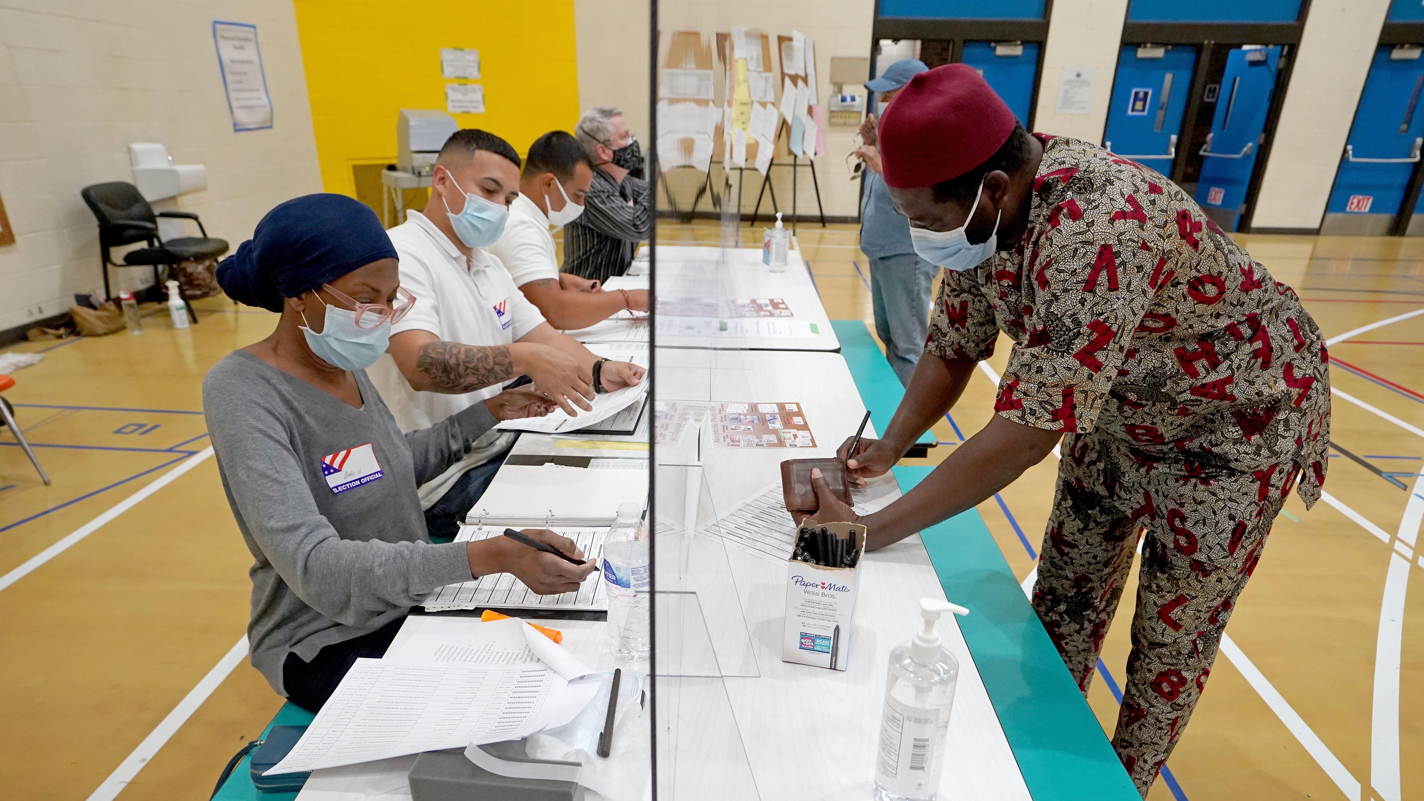 Abudakar Saeed, right, of Milwaukee checks in to vote as he and election inspectors are protected by a plexiglass shield at North Division High School on West Center Street in Milwaukee.