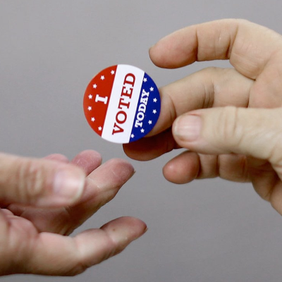 Image of one person putting an "I Voted Today" sticker in another person''s hand
