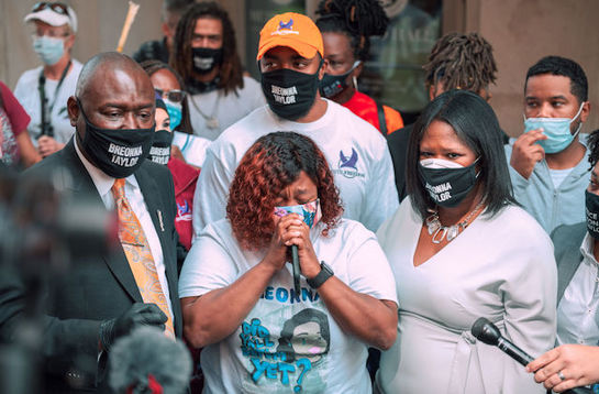 A group of Black people stand around a microphone wearing face masks that read, "Breonna Taylor."