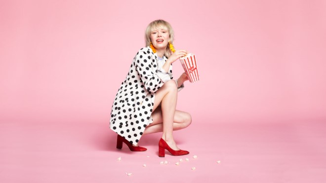 Woman in polka-dot outfit kneeling and eating popcorn