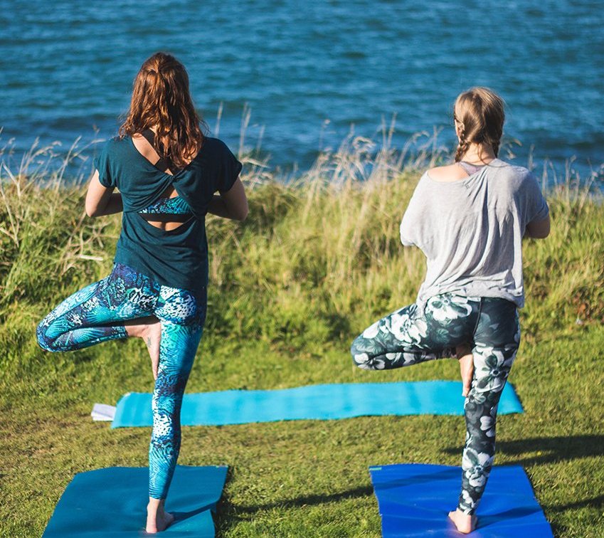Two women practicing Yoga on the cliffs looking out to sea in Cornwall