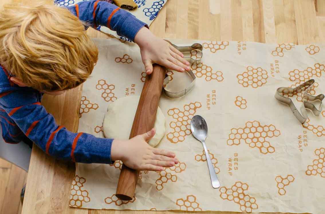young boy rolling cookie dough on top of bee''s wrap with some cookie cutter shapes