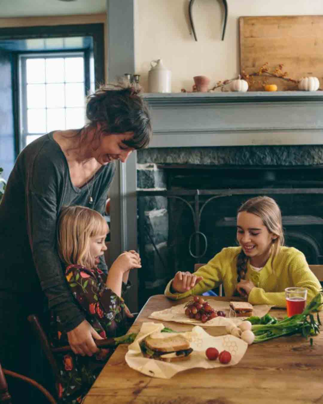 Woman at dining room table with children eating sandwiches on top of bee''s wrap reusable food wraps