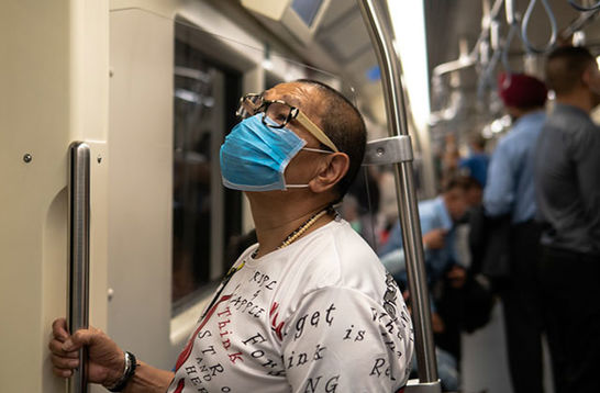 COVID-19. Asian American wearing blue medical mask and white T-shirt stands on train holding pole.